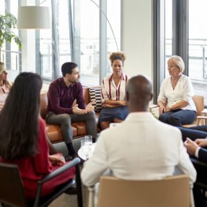 A group of business people in an office in a circle talking