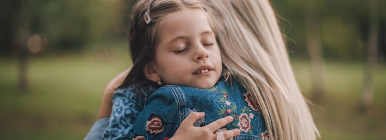 A young child in a blue dress hugging her mother