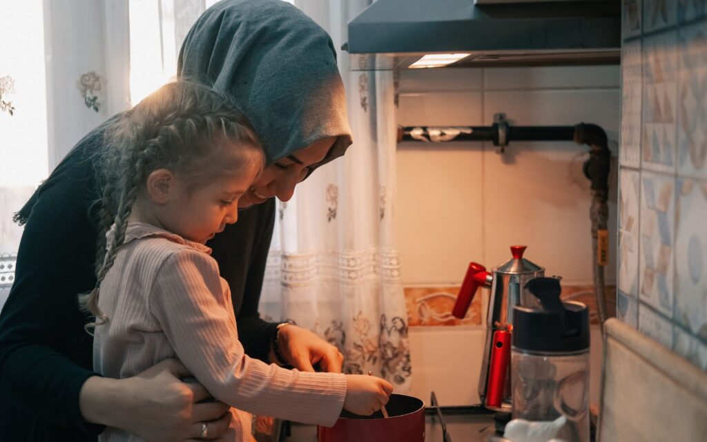 Woman wearing grey head scarf cooking with her young daughter