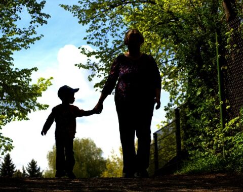 An older woman walking with a young boy through a wood, they are holding hands and cast in shadow