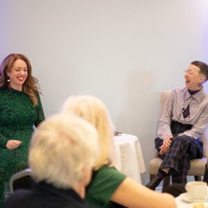 Author Erin Kelly - woman in green dress - laughing at an Oasis event, surrounded by the audience who are also laughing.
