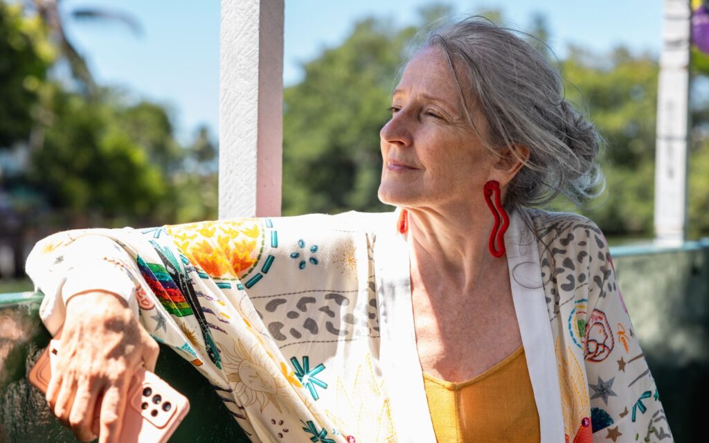 An older woman with grey shoulder length hair sat outdoors staring in the distance