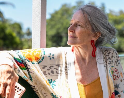 An older woman with grey shoulder length hair sat outdoors staring in the distance