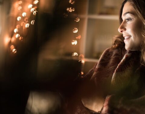 A woman smiling sitting down infront of a Christmas tree and fairy lights