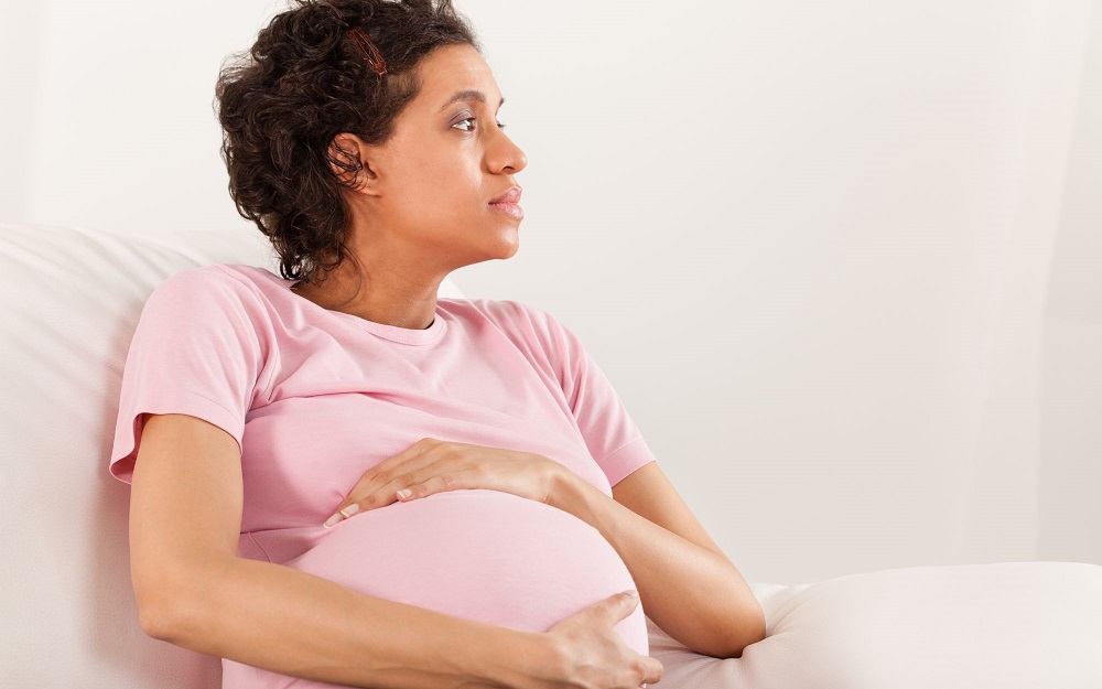 A pregnant woman with curly hair wearing a pink t shirt, holding her pregnant belly