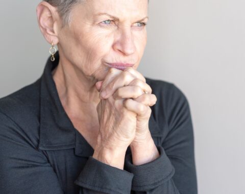An older woman with hands helf together under her chin, staring into the distance