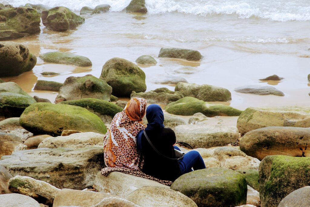 Two women sat on beach rocks comforting each other looking out to sea