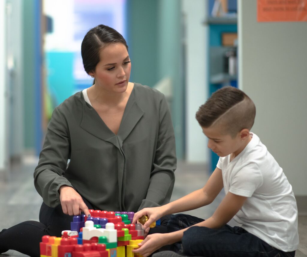 A mother sitting on the floor with her soon playing wiith a toy and looking concerned.