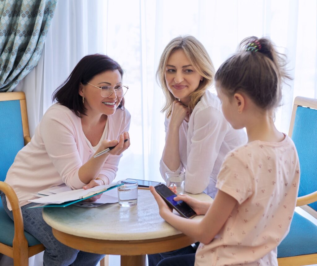 A support worker talking to a mother and daughter around a table.
