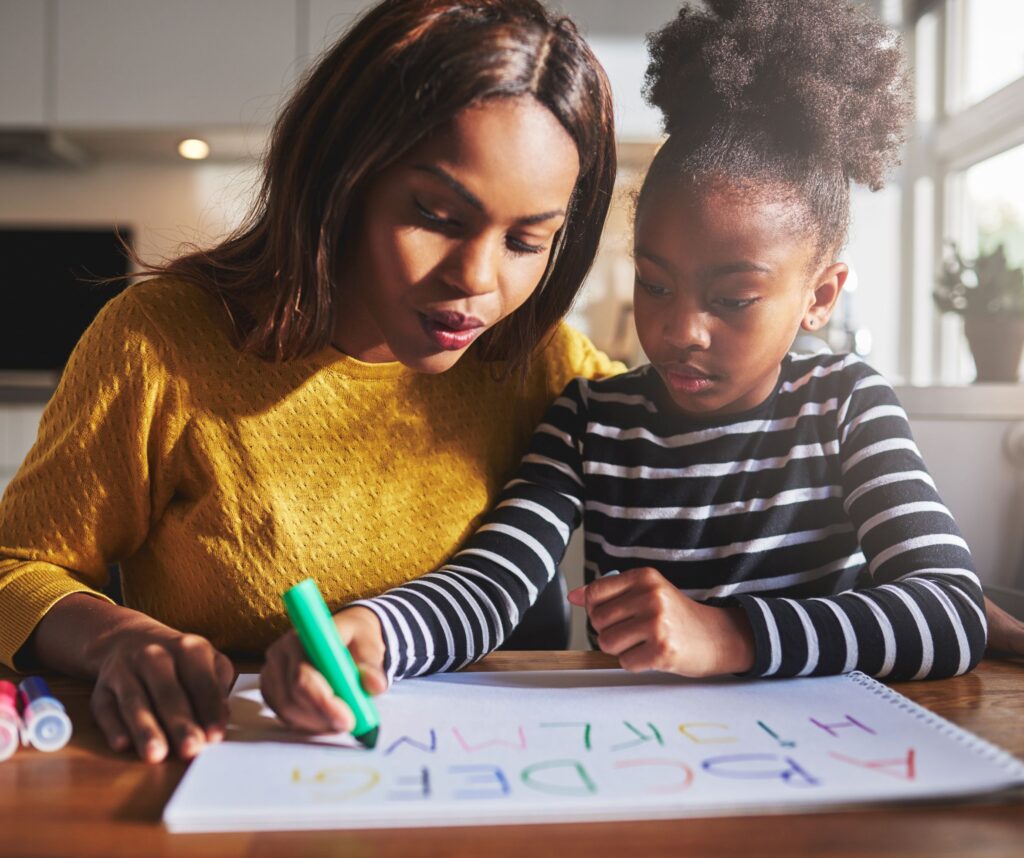 A woman with her daughter at a kitchen table drawing.