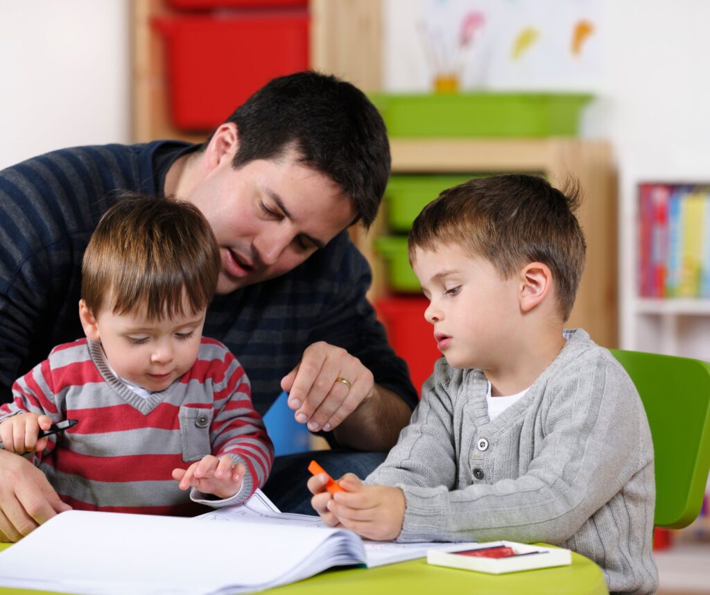 A father with his two young sons drawing in a playroom.